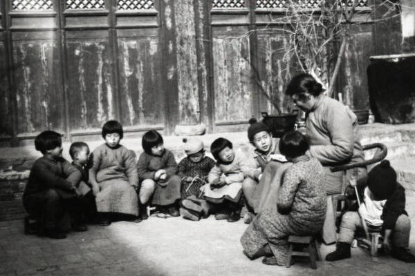 Woman reading to group of nine children sitting on the ground of a courtyard